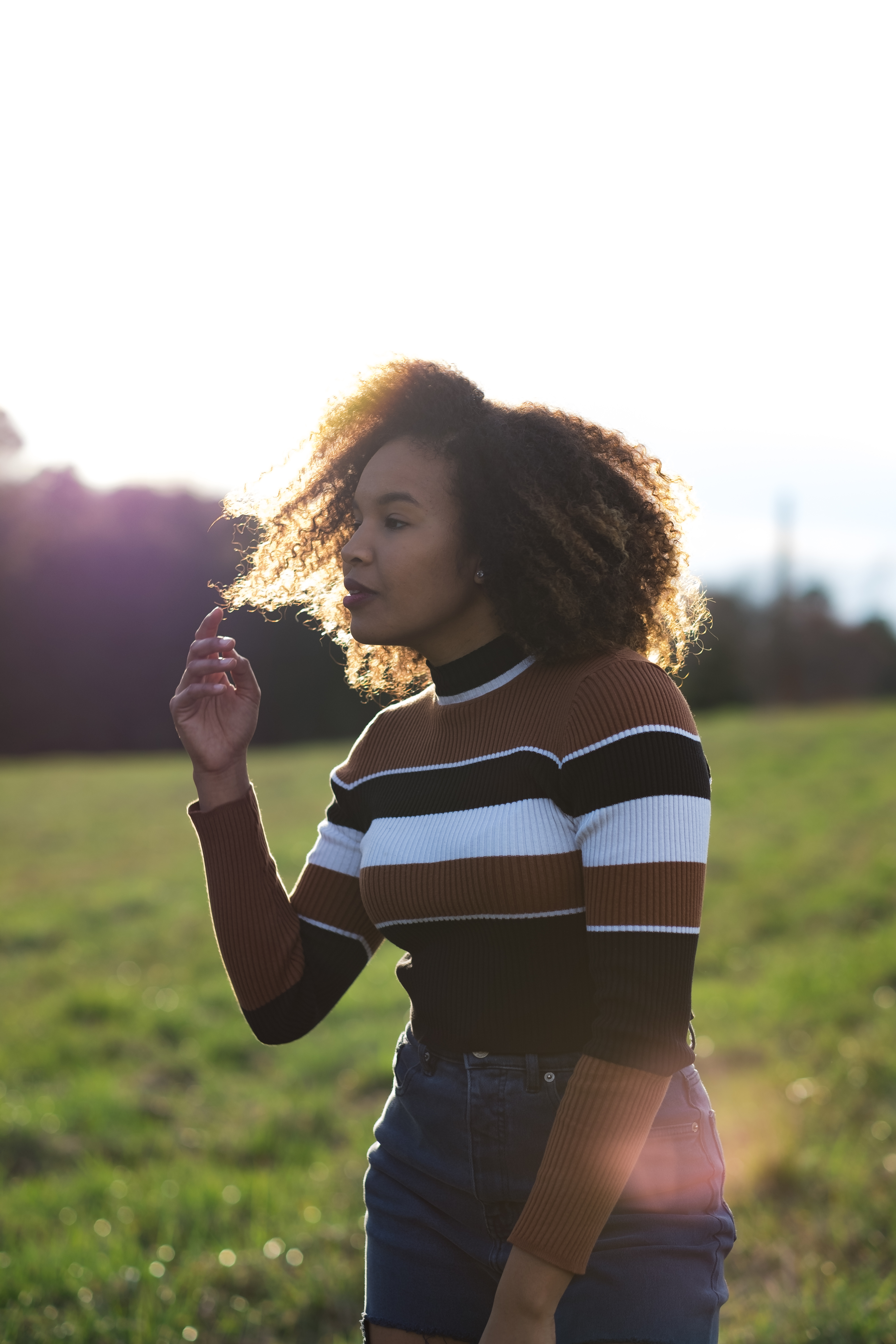 Portrait of a woman in striped sweater lit from behind in an open field