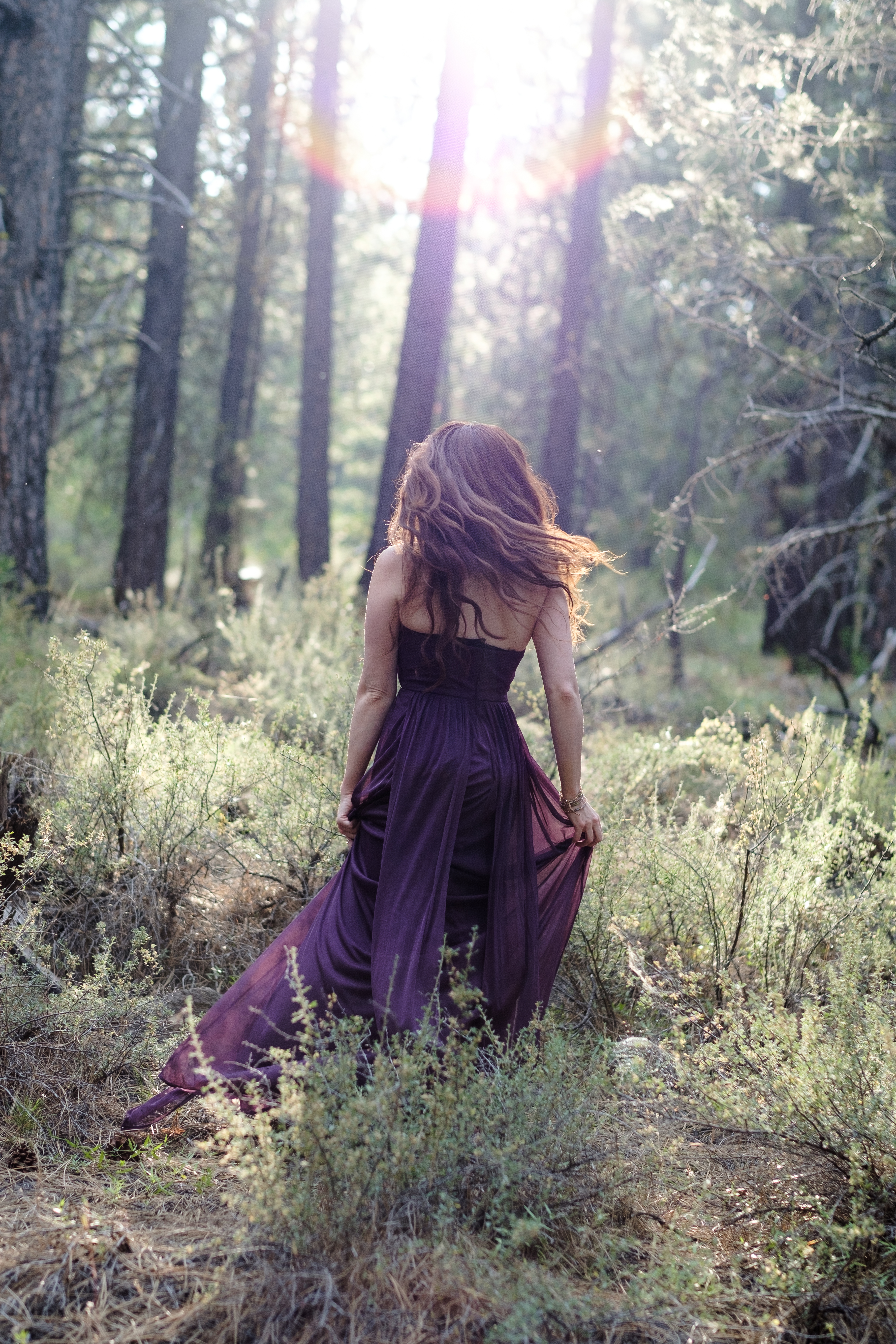 Woman in a plum dress moving through a sunlit forest